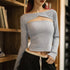 Person wearing a gray long-sleeve crop top with cut-out design in a room with wooden shelves.